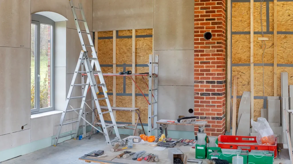 Eine Baustelle in einem Altbau, bei der Wände mit Trockenbau und Innendämmung verkleidet werden, davor stehen eine Leiter und Werkzeuge.